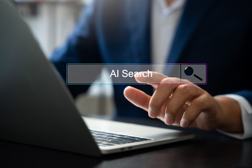 Person tippt auf eine Suchleiste mit der Aufschrift AI Search vor einem Laptop